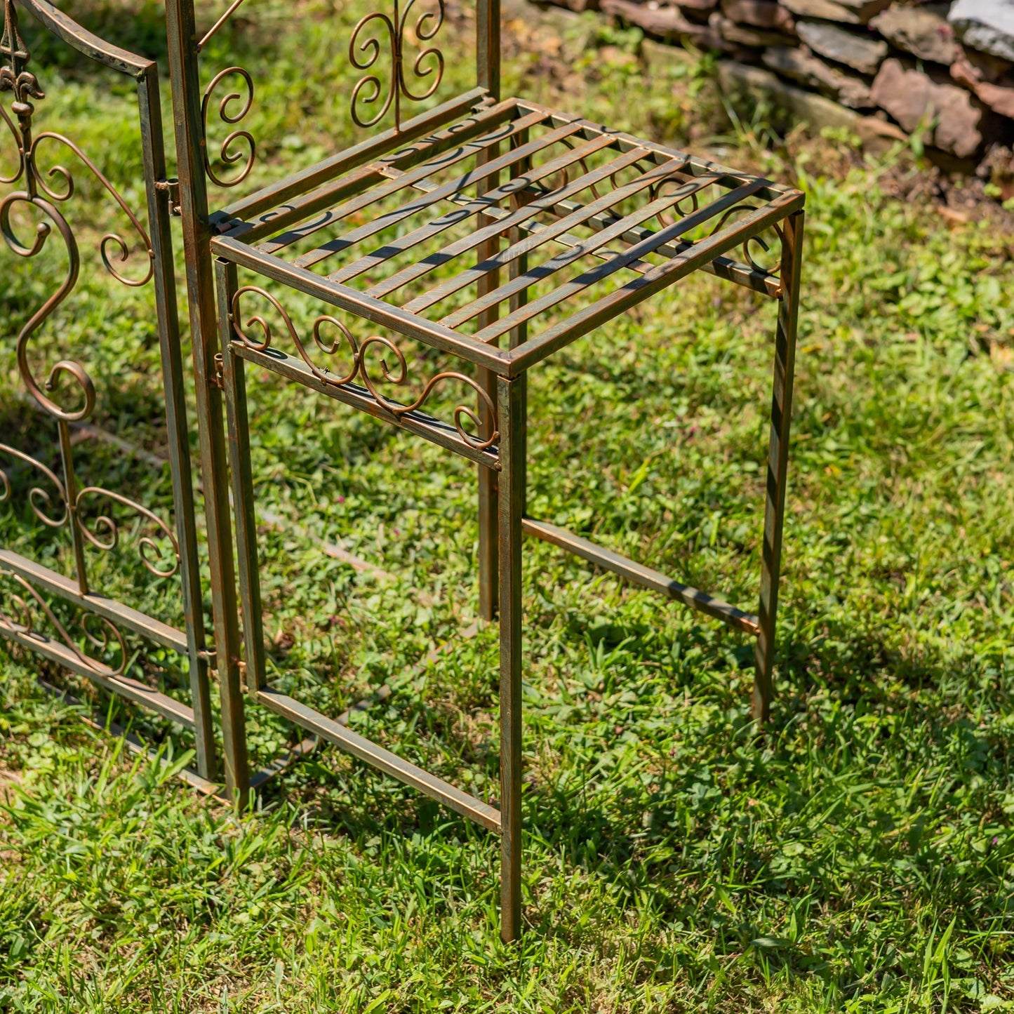 Decorative metal plant stand on grass with a stone wall in the background