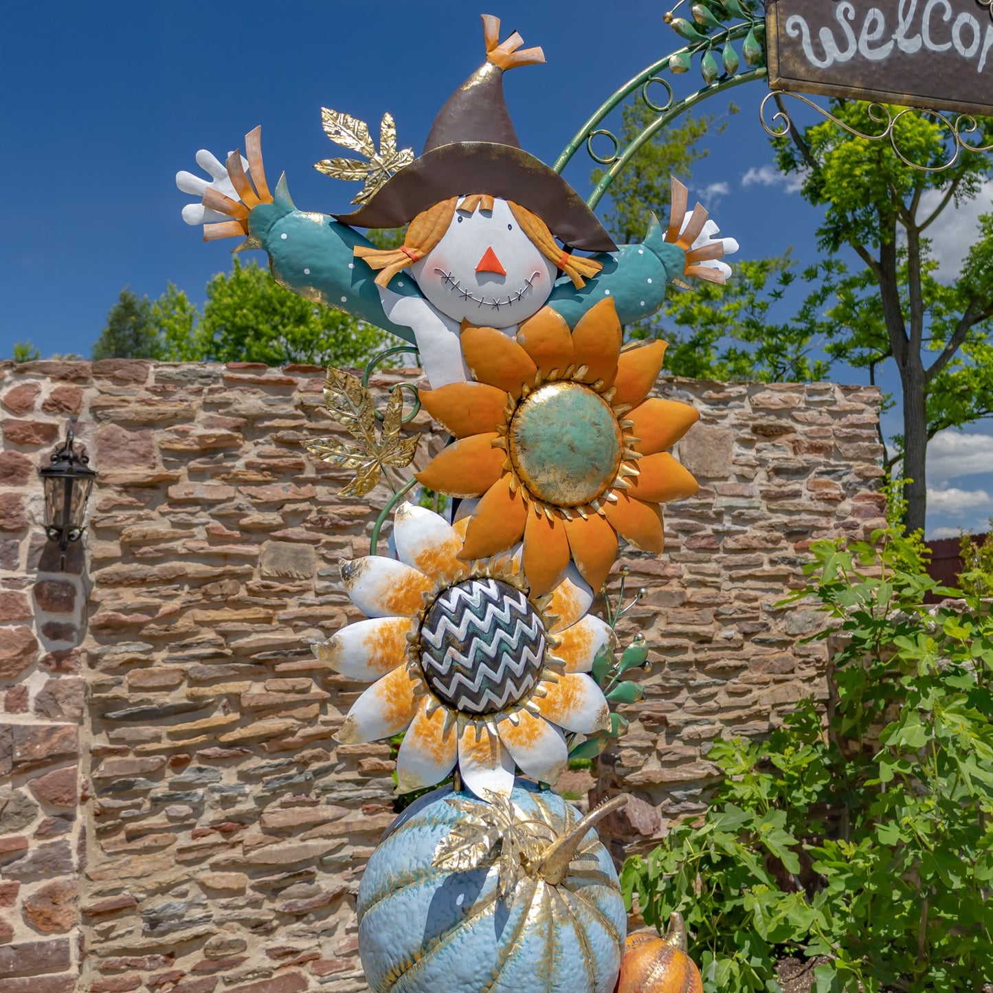 Decorative scarecrow with flowers against a stone wall and blue sky
