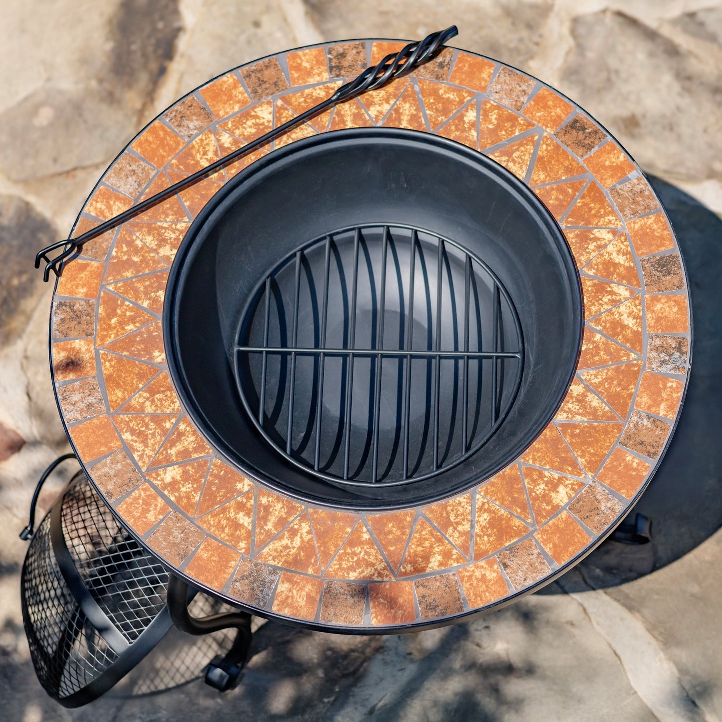 Fire pit with mosaic stone design and black metal grate on a stone surface