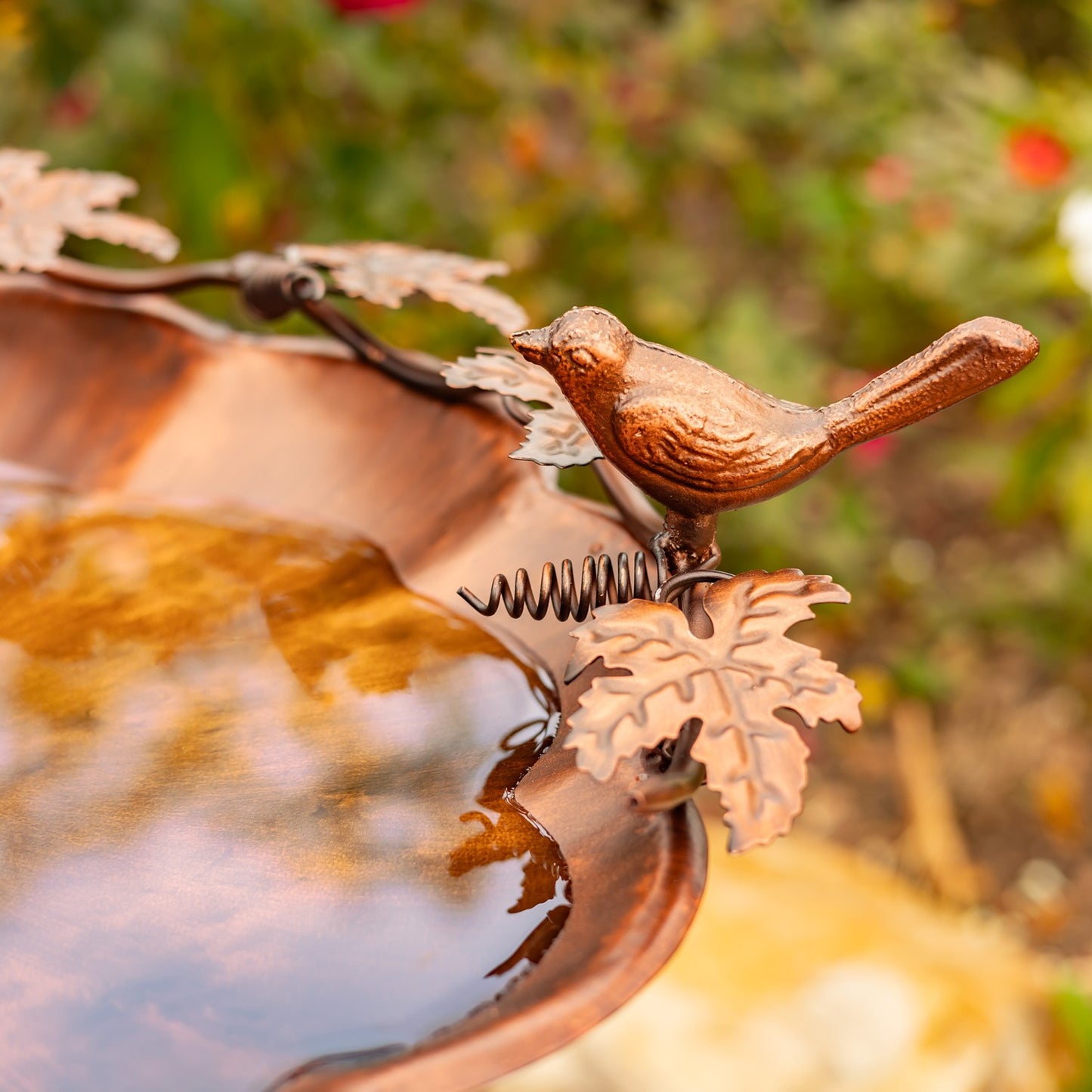 Flower shaped birdbath with ivy and birds sitting on the side in a garden setting
