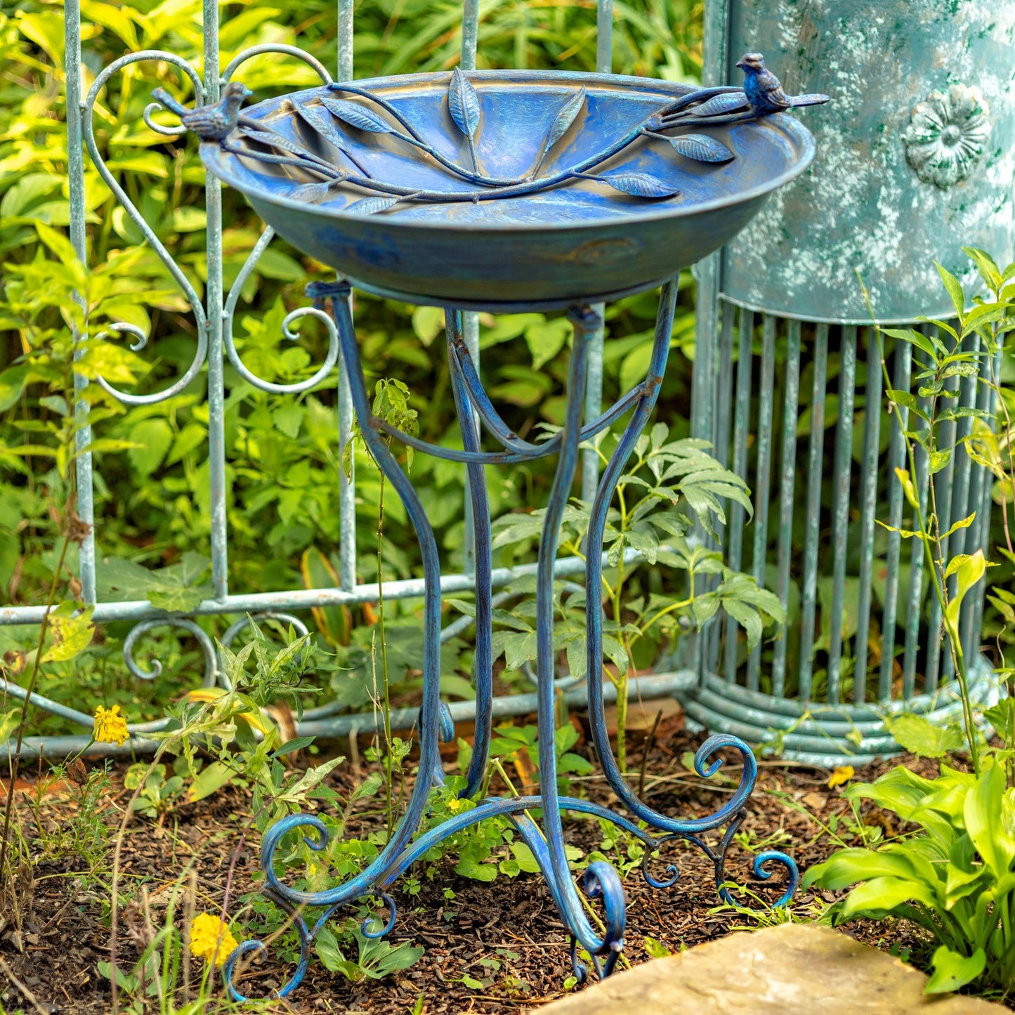 Decorative blue metal bird bath with stand in a garden setting