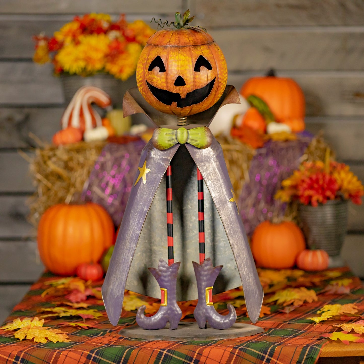 Halloween-themed decorative figure with a jack-o'-lantern head on a table with pumpkins and autumn decorations.