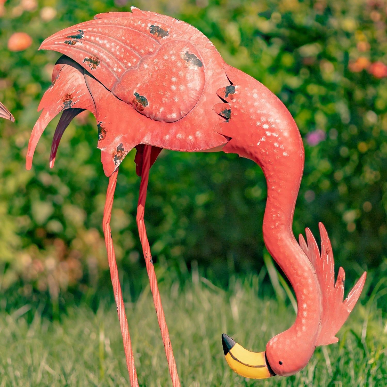 A pink flamingo garden stake decoration with a yellow beak, photographed outdoors in a grassy garden setting.