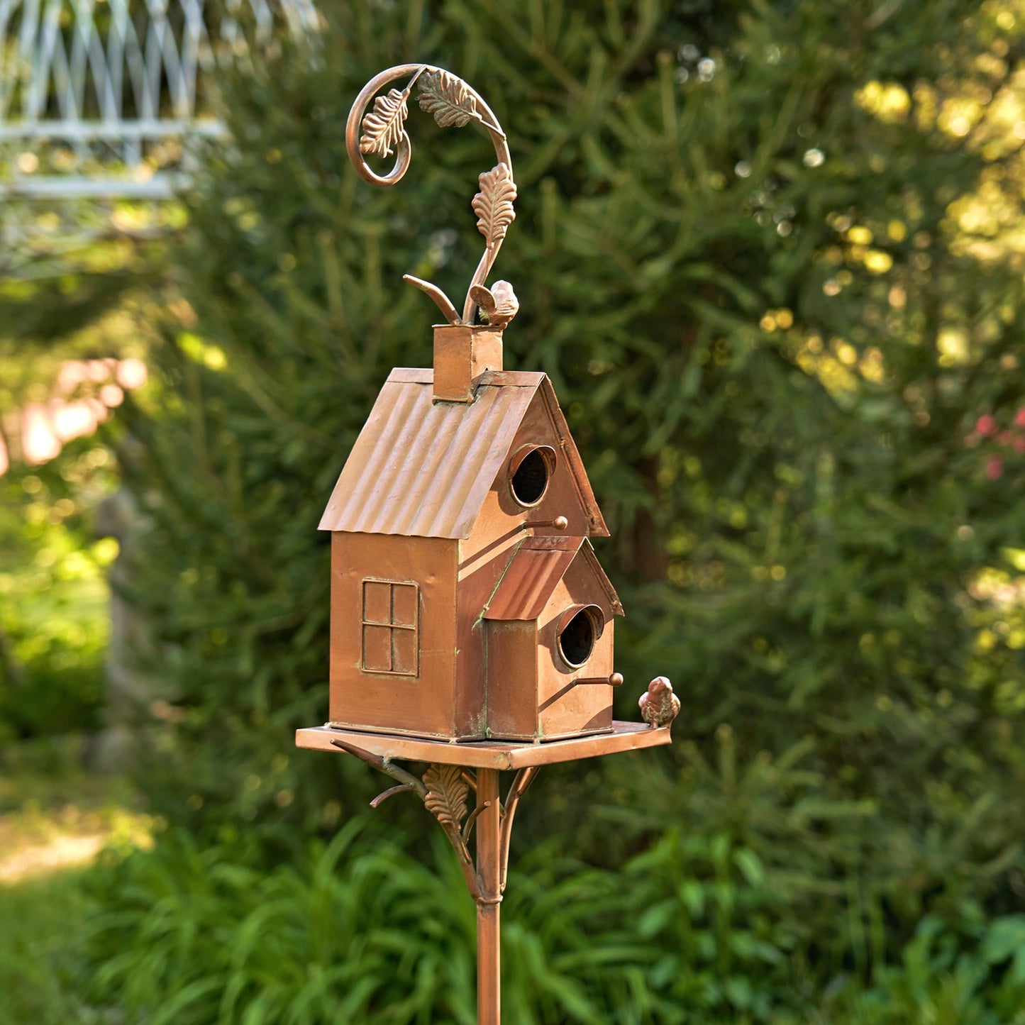 Decorative copper birdhouse on a stand with a garden background
