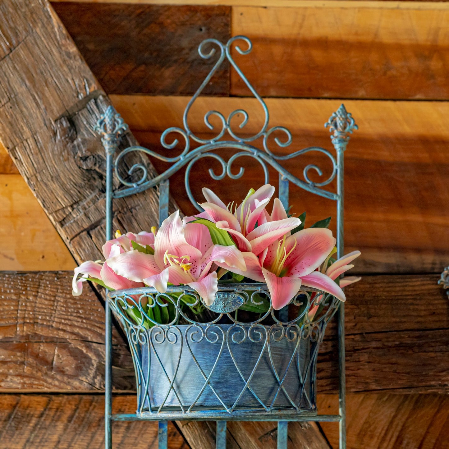 Decorative metal plant stand with pink flowers against a wooden background