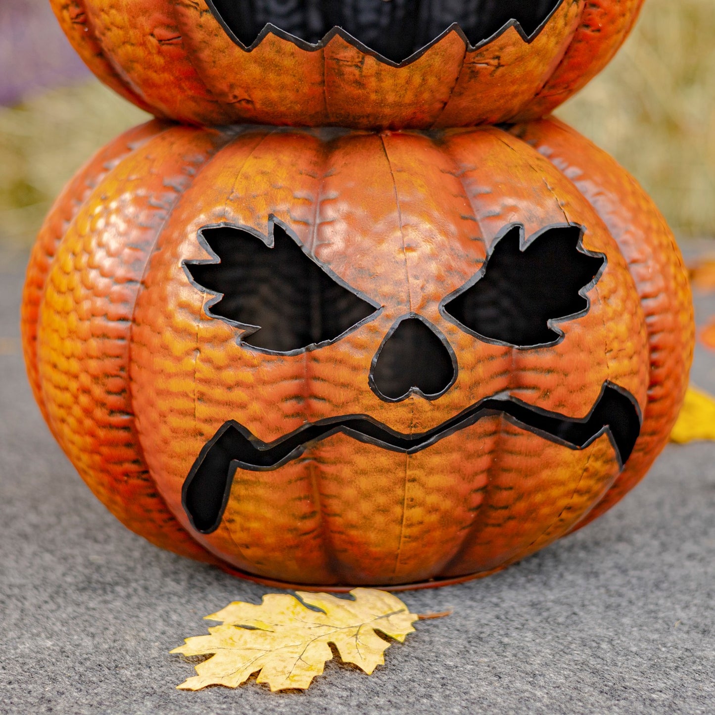 Two stacked pumpkins with a carved face on a gray surface