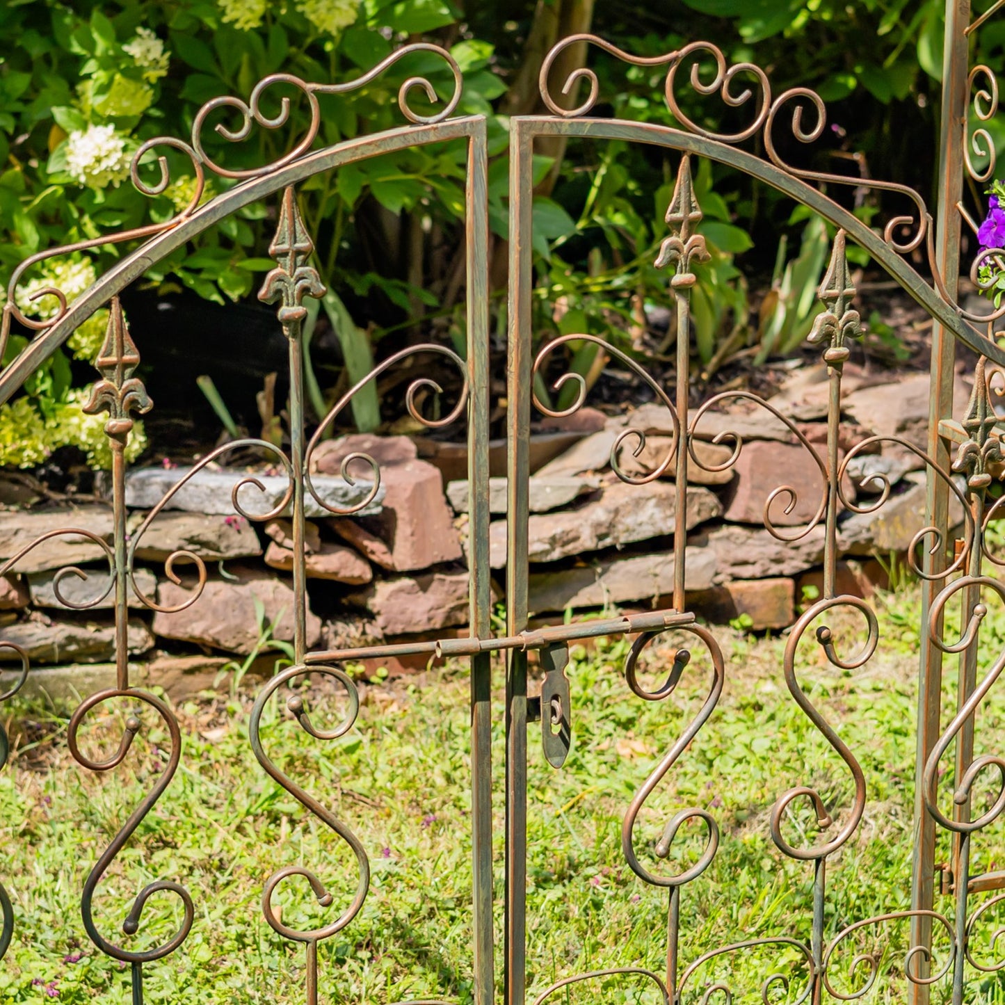 Decorative metal garden gate with intricate designs in a garden setting.