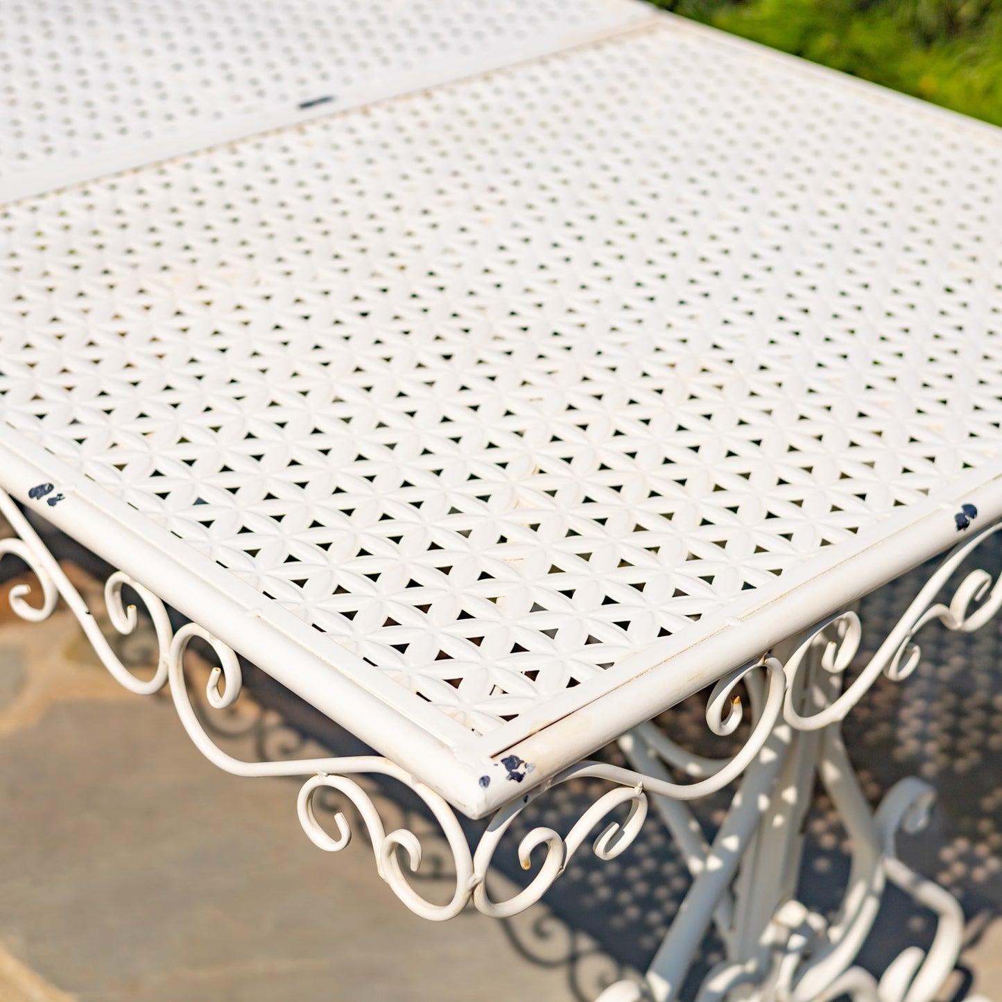 White metal garden table with decorative lattice design on a blurred outdoor background