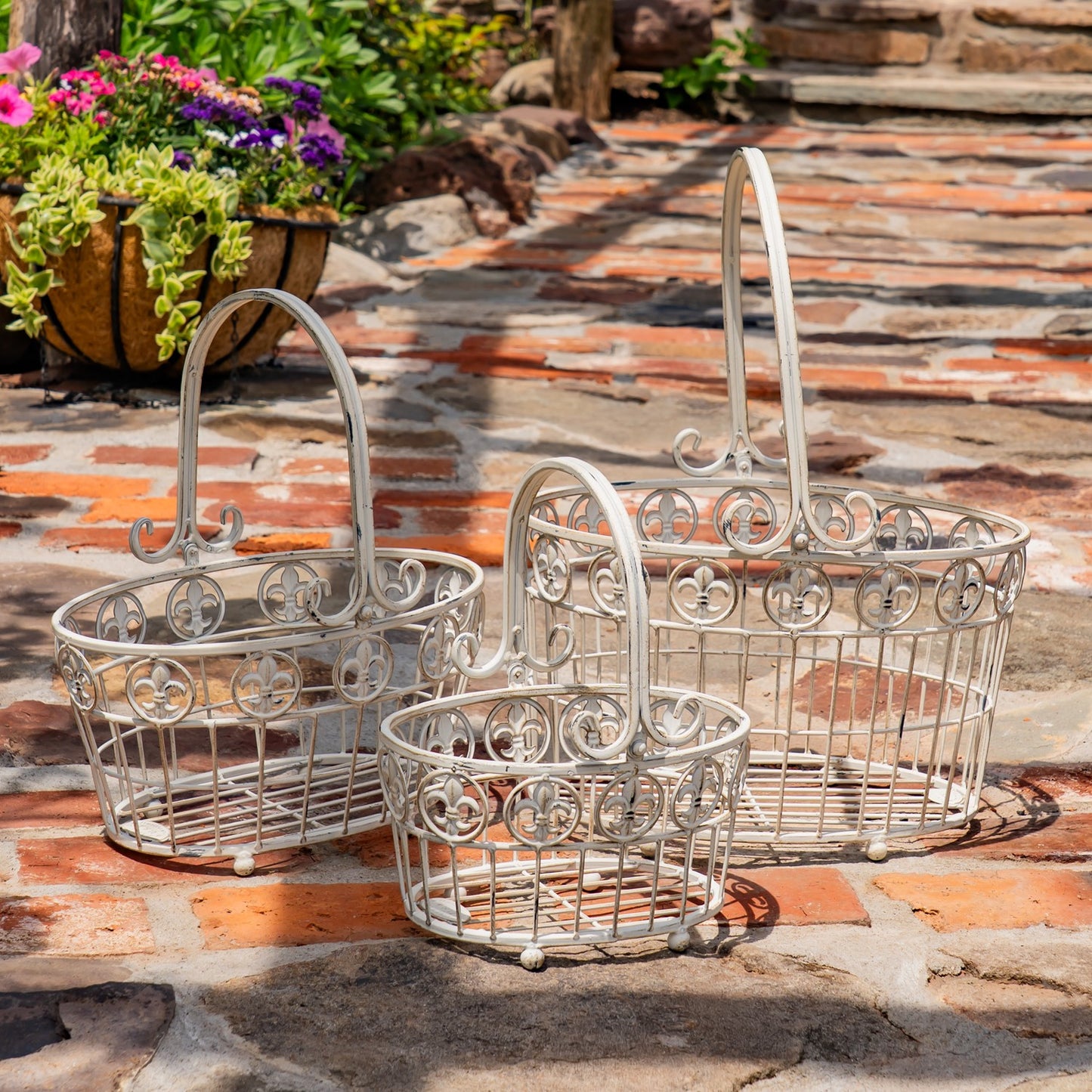 Three decorative metal garden baskets in different sizes arranged on a stone patio with a potted plant in the background.