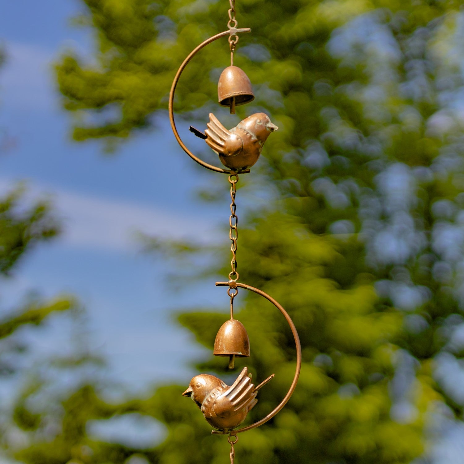 Decorative wind chime with birds and bells against a blurred green background