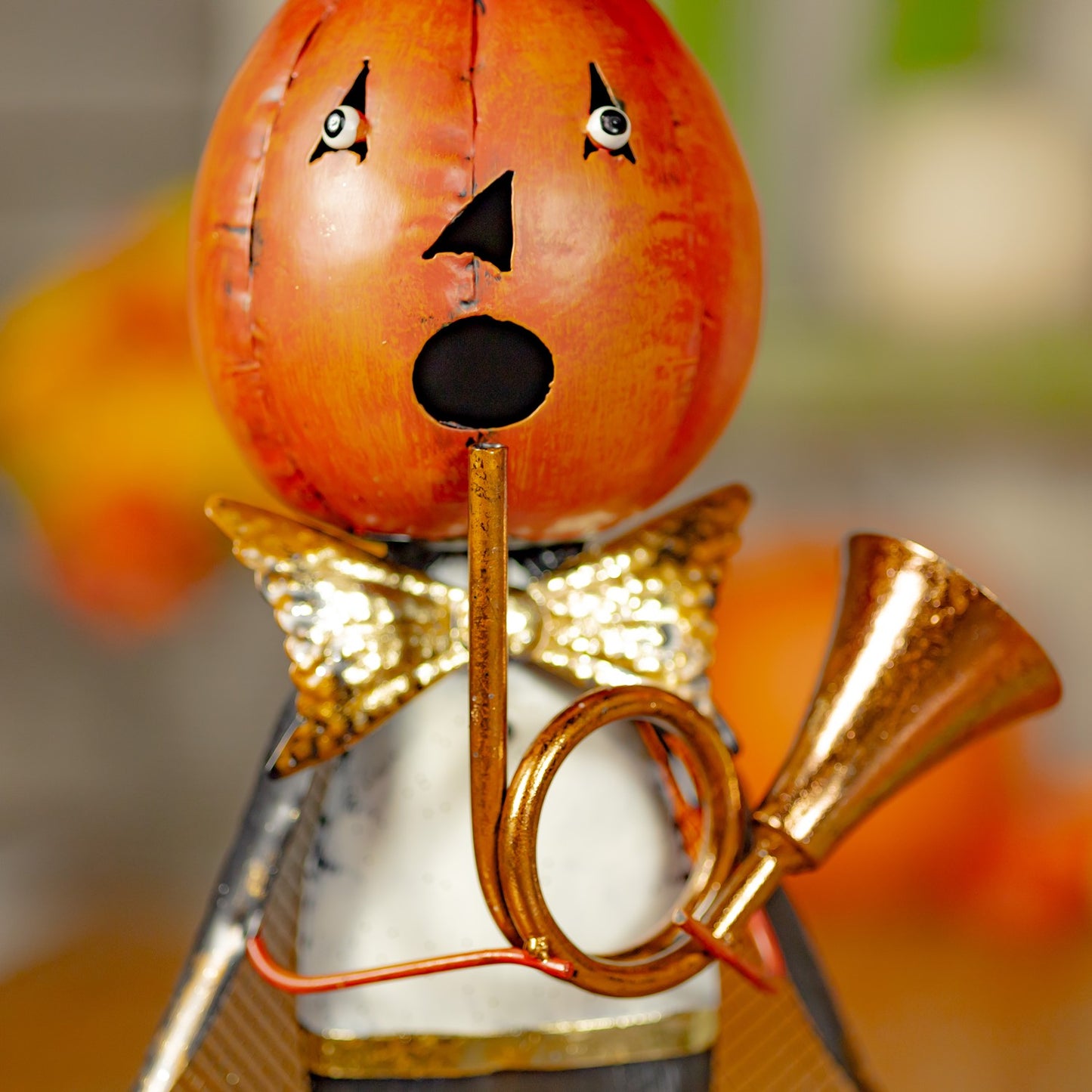 Decorative figure with a pumpkin head and gold outfit blowing a horn, set against a blurred background.