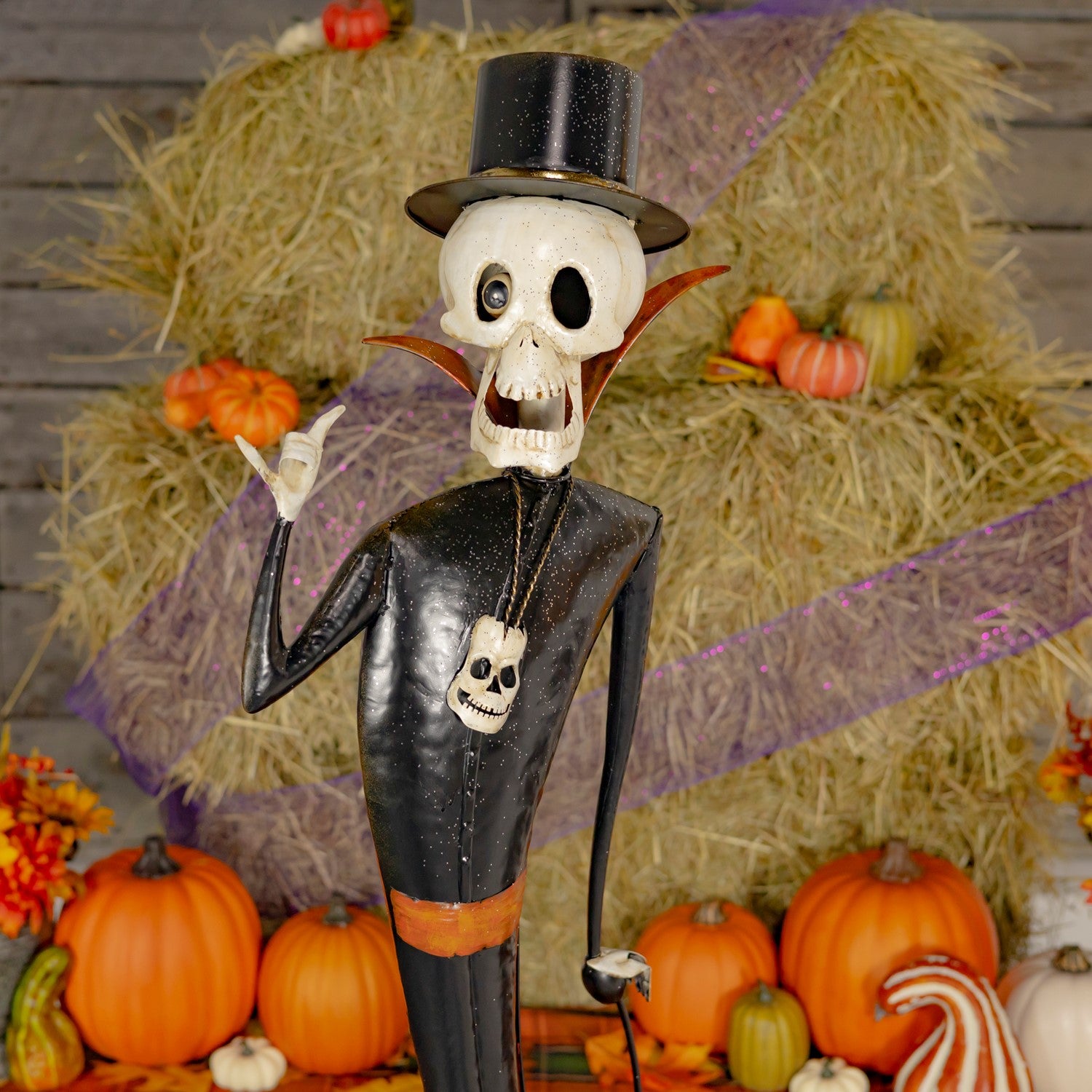 Skeleton figure in formal attire with a top hat surrounded by pumpkins and hay bales.