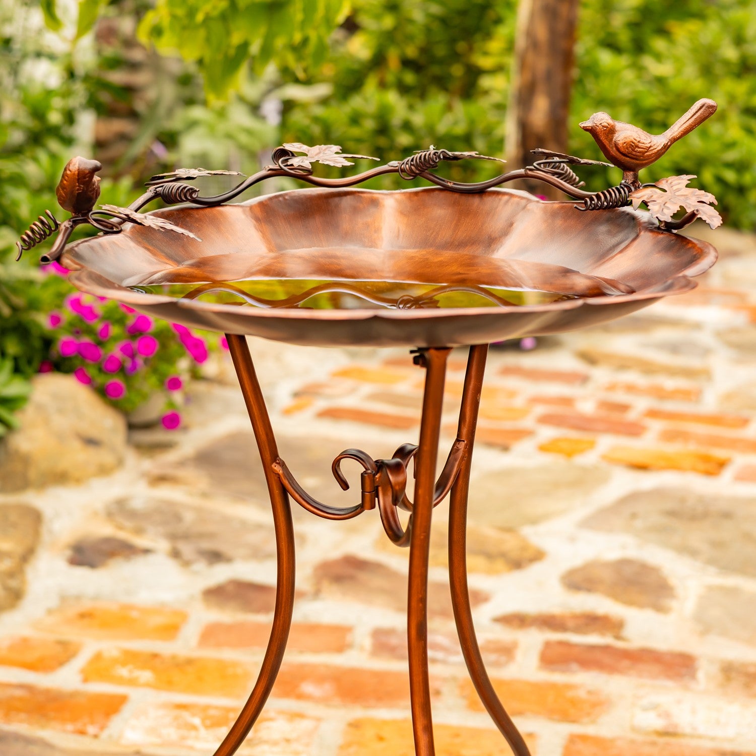 Flower shaped birdbath with ivy and birds sitting on the side in a garden setting