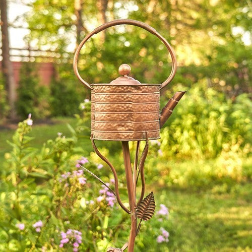 Decorative copper watering can with a garden background