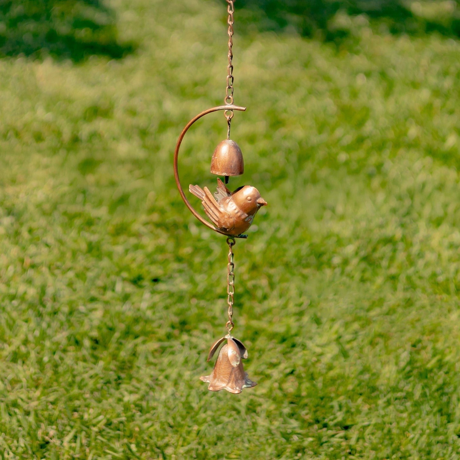 Decorative wind chime with birds and bells against a blurred green background