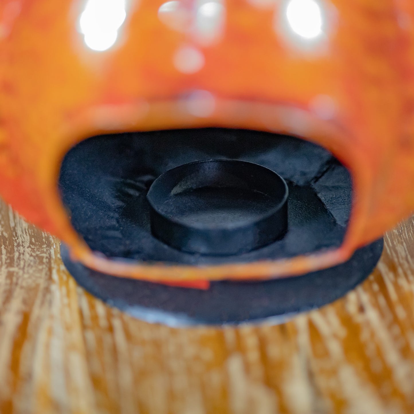 Close-up of an orange decorative object with a black circular insert and black textured base, photographed on a wooden surface.