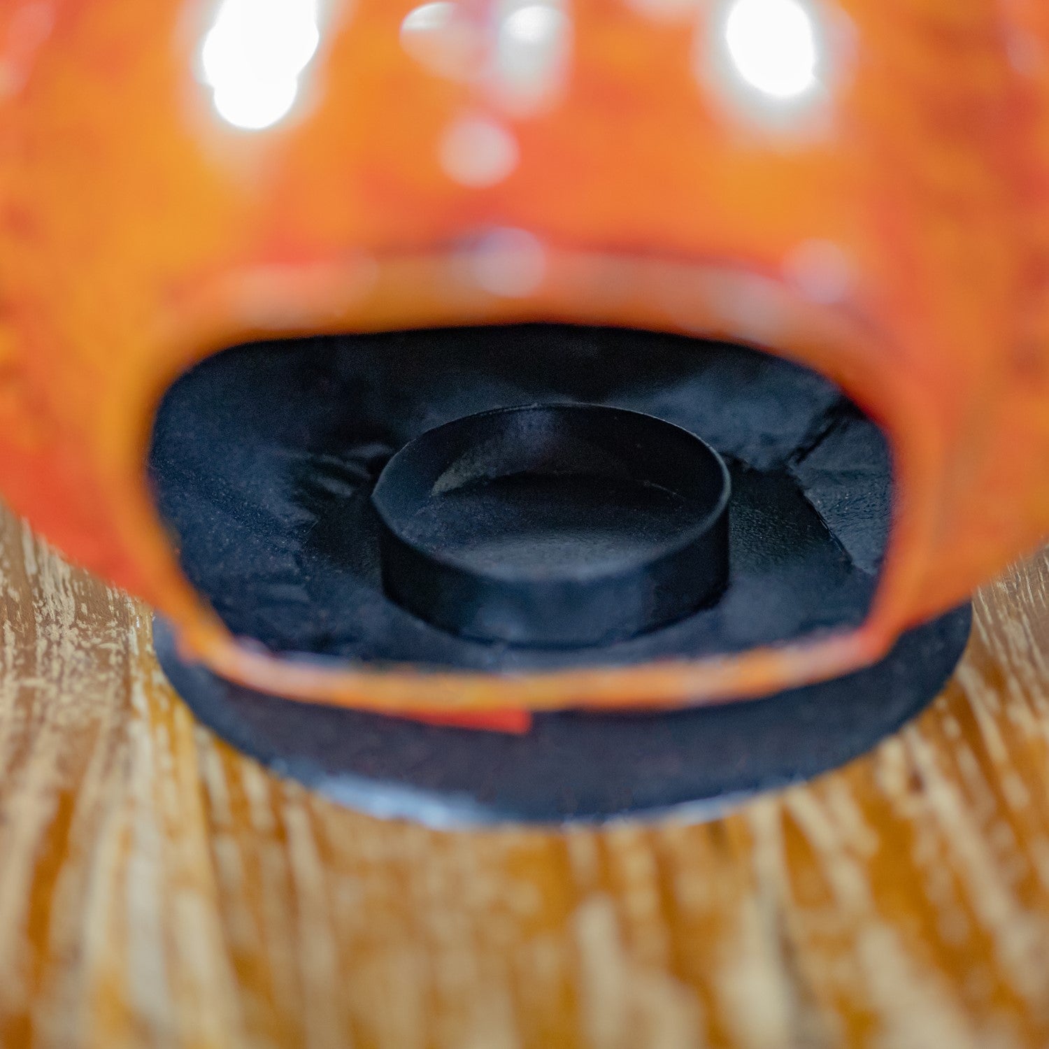 Close-up of an orange decorative object with a black circular insert and black textured base, photographed on a wooden surface.