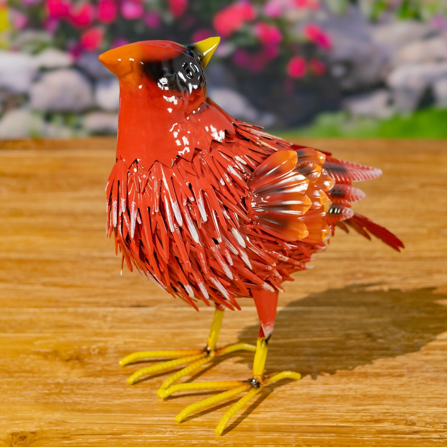 Red cardinal bird figurine on a wooden surface with blurred flowers in the background