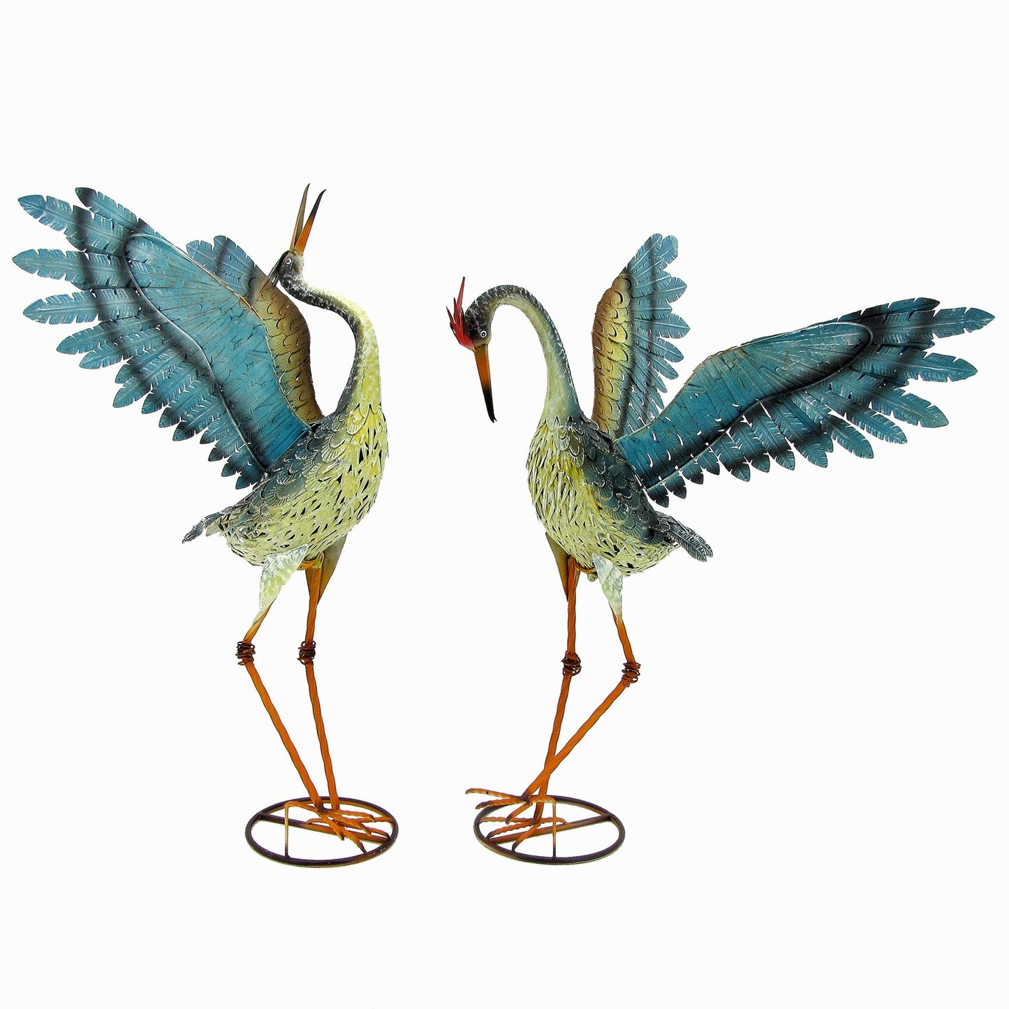 Two decorative metal cranes facing each other, each with spread blue and teal wings, speckled yellow-green bodies, orange legs, and small red crests, mounted on circular wire bases against a plain white background.