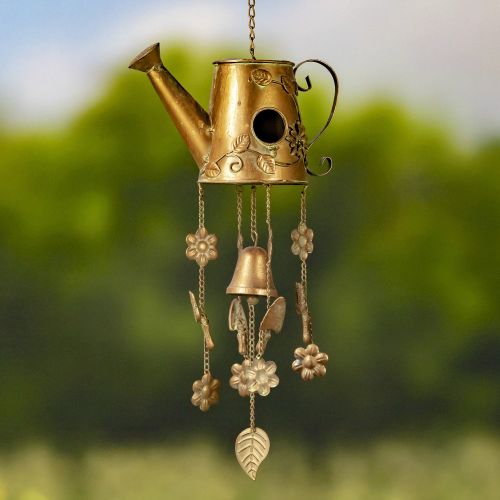 Decorative brass watering can with hanging elements against a blurred green background