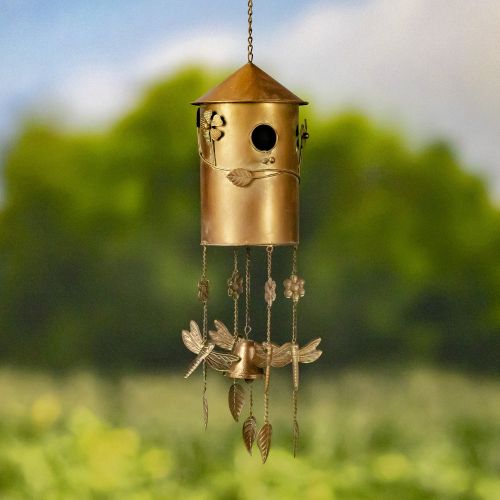 Decorative brass wind chime with floral and dragonfly designs against a blurred natural background.