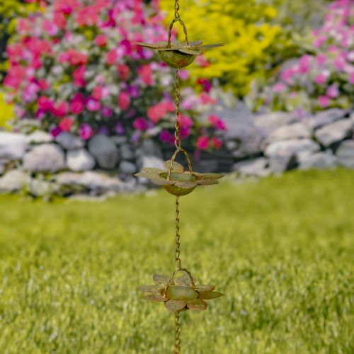 Decorative wind chime with floral designs hanging against a garden background with flowers and rocks.