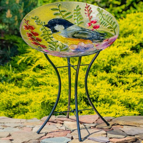 Decorative bird bath with a painted bird and floral design on a stand, set against a natural background.
