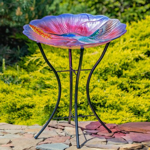 Colorful glass bird bath on a metal stand with a garden background