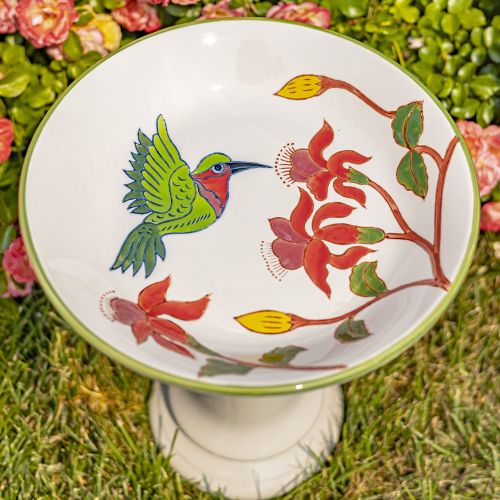 Ceramic bird bath with a colorful design of a hummingbird and flowers on a grassy background.