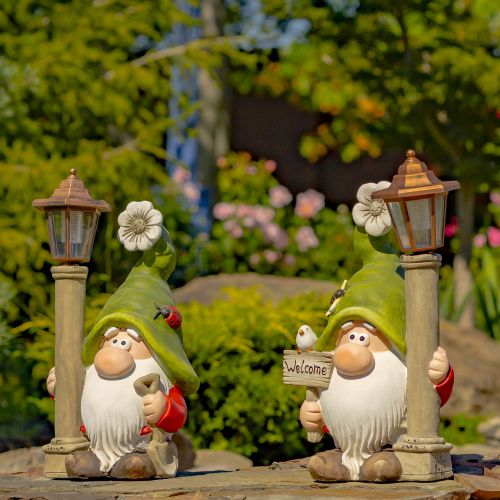 Two garden gnomes with lanterns and a sign in a garden setting