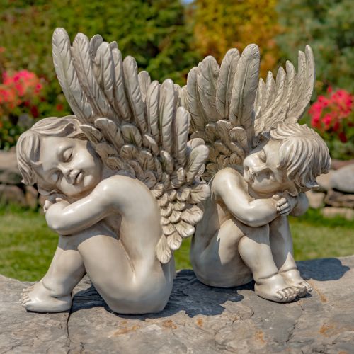 Two stone angel statues with wings on a rock with a garden background