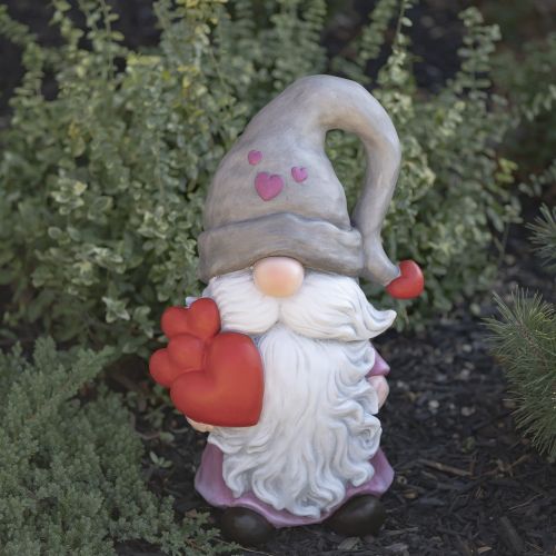 Gnome figurine with a heart-shaped gift in front of green bushes