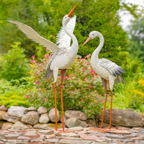 Two decorative storks on a stone pathway with a garden background