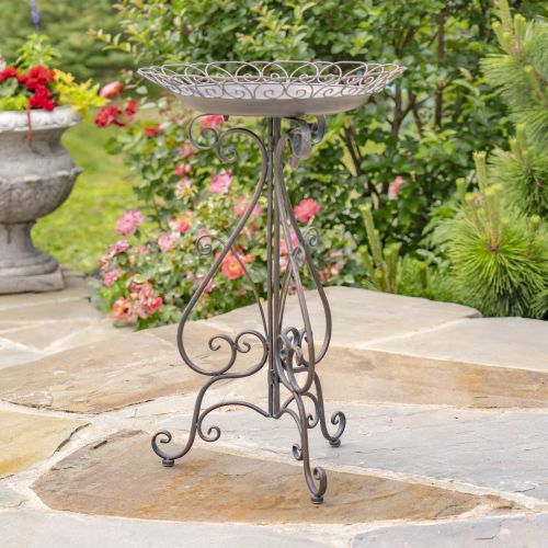Decorative metal stand on a stone patio with garden flowers in the background