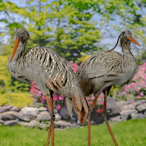 Two decorative bird sculptures in a garden setting with flowers and rocks in the background.