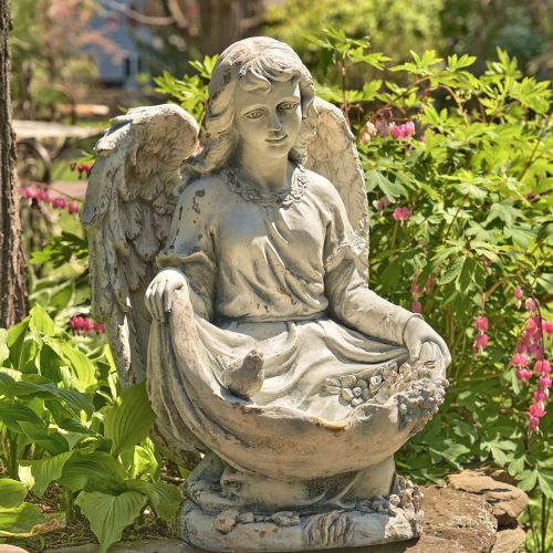 Stone angel statue in a garden setting with greenery and flowers.
