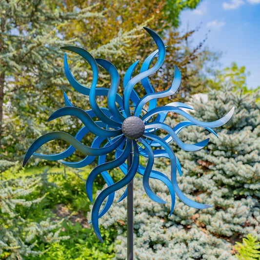 Blue metal windmill in a garden setting with trees and sky in the background